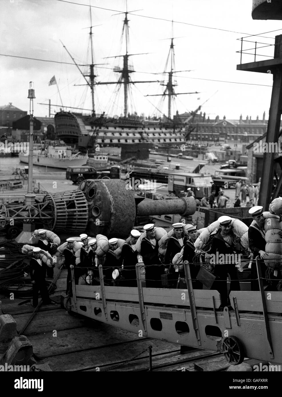 Sailors of the British Navy board the aircraft carrier 'Warrior' at Portsmouth. They are to relieve sailors already on duty in the Far East waters. In the background is H.M.S. Victory. Stock Photo