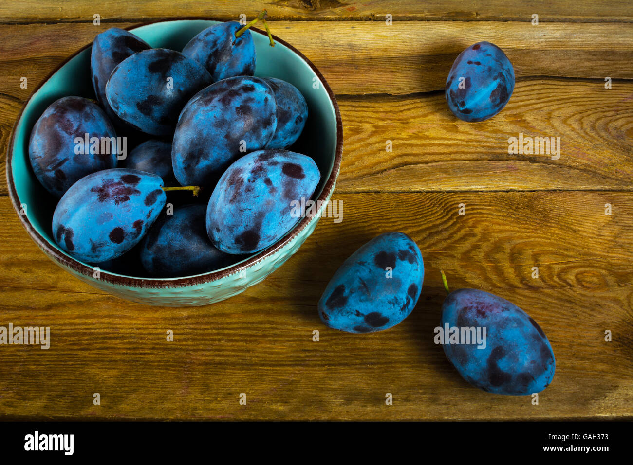 Fruit plums prunes in turquoise cup on the old dark wooden background top view. Selective focus Stock Photo