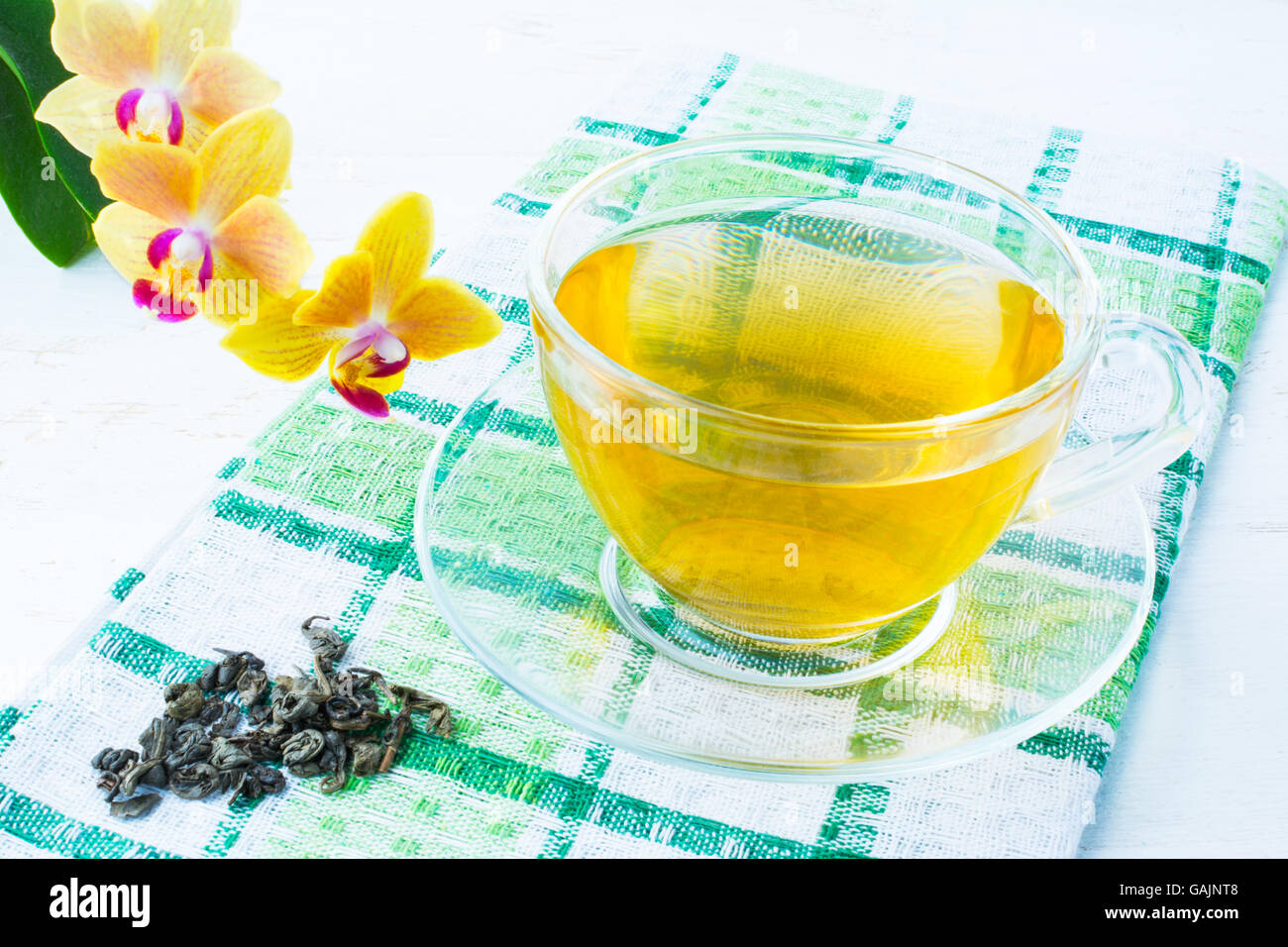 Cup of green tea on green checkered napkin with a yellow orchid on a white wooden background. Cup tea. Cap of tea. Tea.  Green t Stock Photo