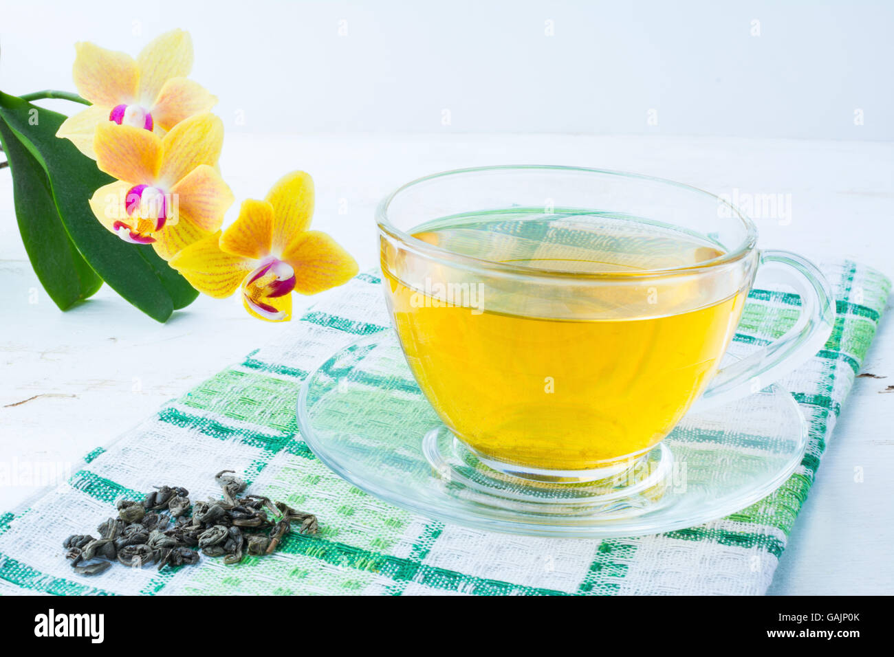 Cup of tea on green checkered napkin with a yellow orchid on a white wooden background. Cup tea. Cap of tea. Tea.  Green tea.  T Stock Photo