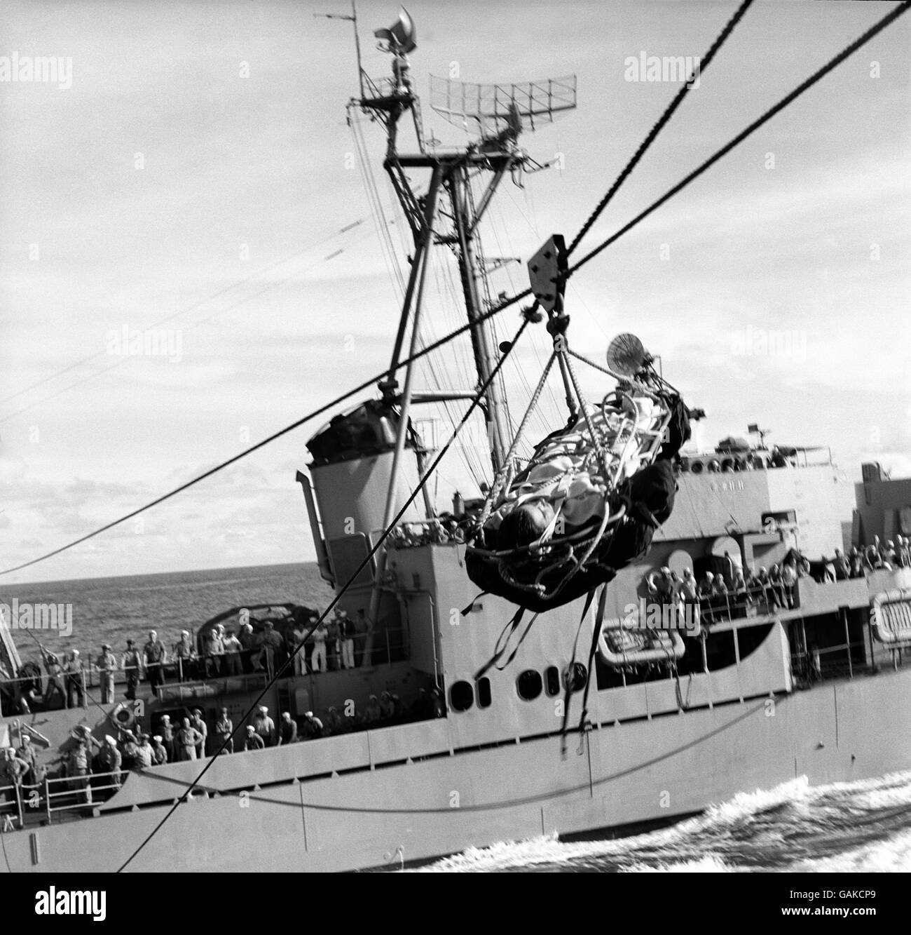 Strapped to a stretcher swinging over the ocean, an American seaman taken ill aboard a United States destroyer escorting a convey to Korea- is transferred to a flagship for treatment, the ship did not slacken their 15 knots speed while the tranfer was made. A short while after the seaman was operated on and recovered. Stock Photo
