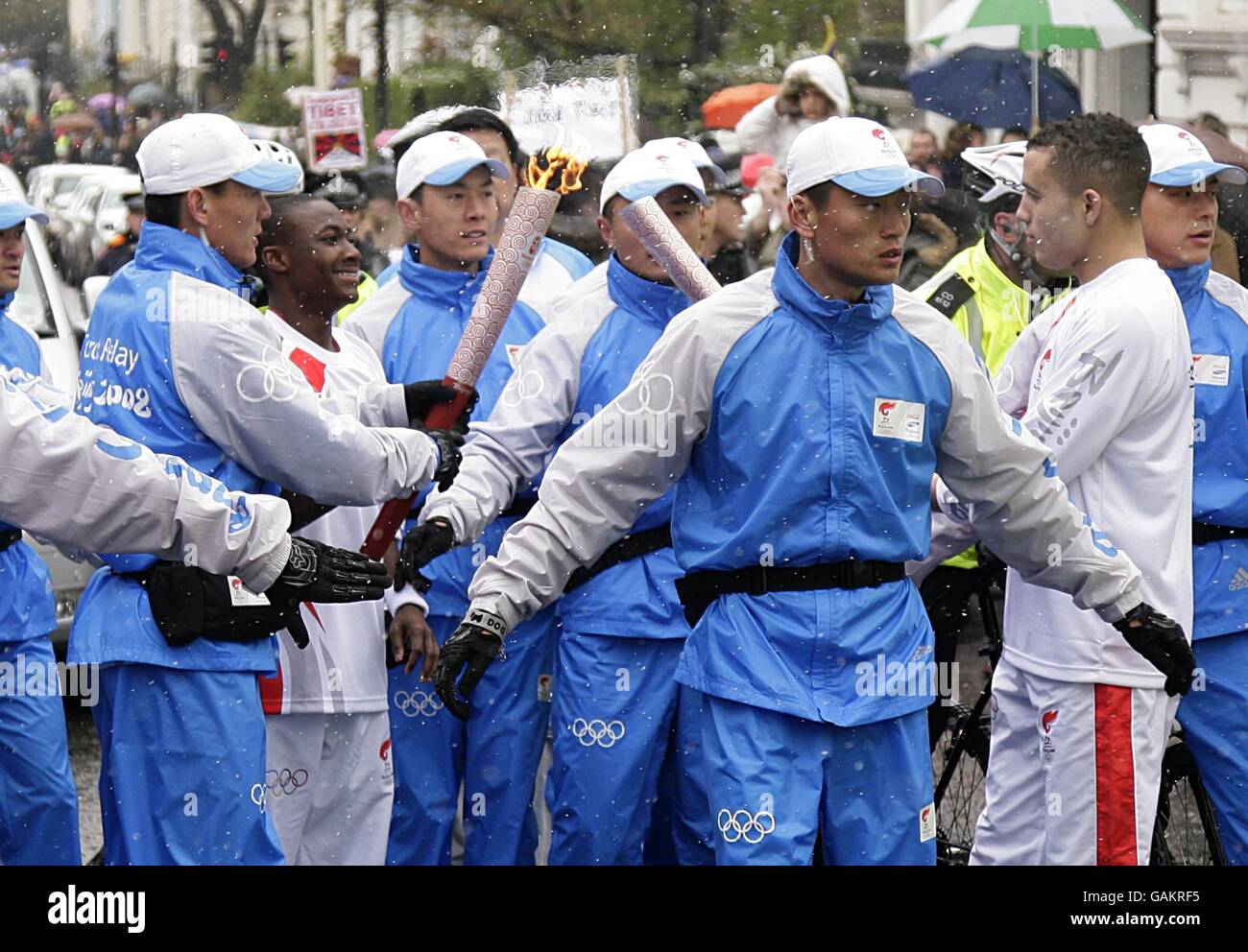 The torch is passed from one runner to the other as the route nears Notting Hill the Beijing Olympics torch relay, heading towards Blenheim Cresent in London. Stock Photo