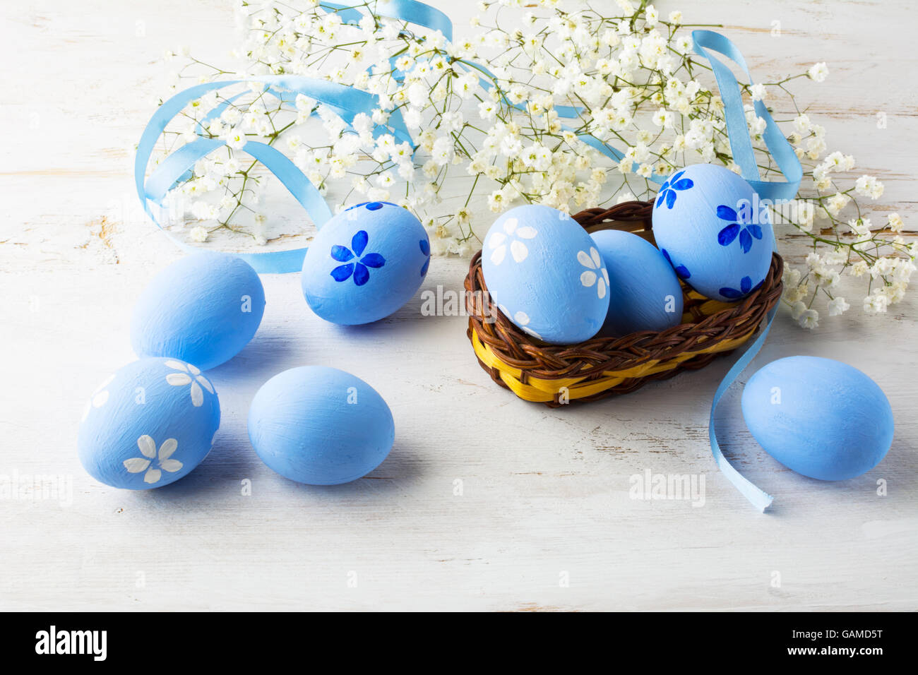 Blue Easter eggs in a small wicker basket and small white baby's breath flowers on white wooden background Stock Photo
