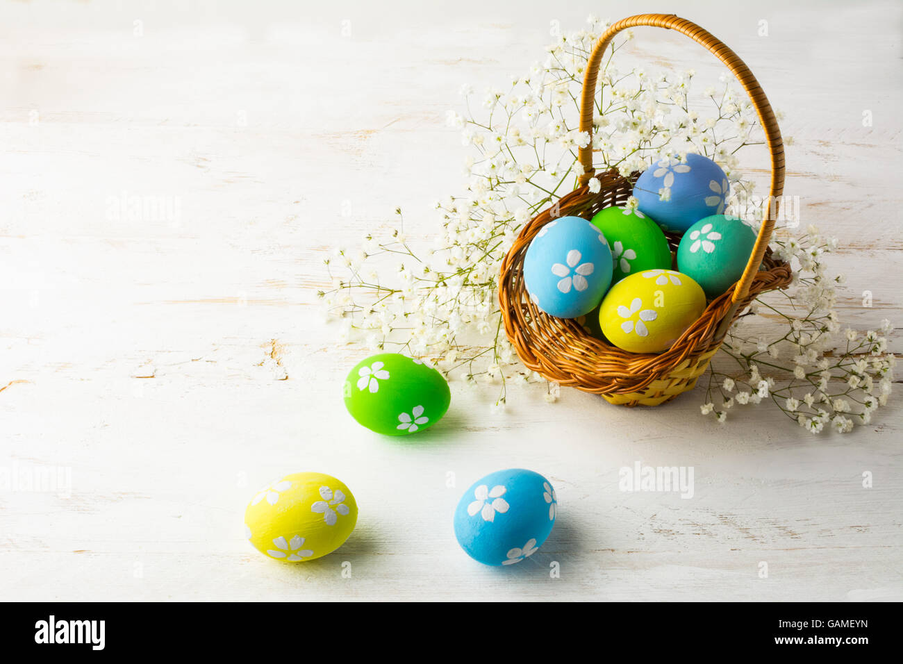 Decorated Easter eggs in the basket with small white baby's breath flowers on a white wooden background, space for text, copy sp Stock Photo