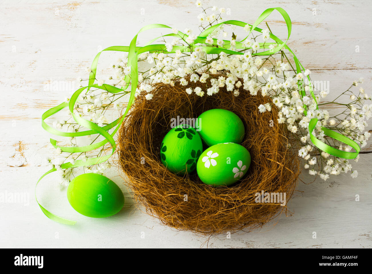 Green Easter eggs in a nest with green satin ribbon and small white baby's breath flowers on a white wooden background, top view Stock Photo