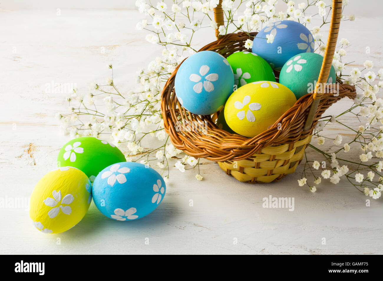 Hand-painted decorated Easter eggs in the basket with small white baby's breath flowers on a white wooden background, close up Stock Photo