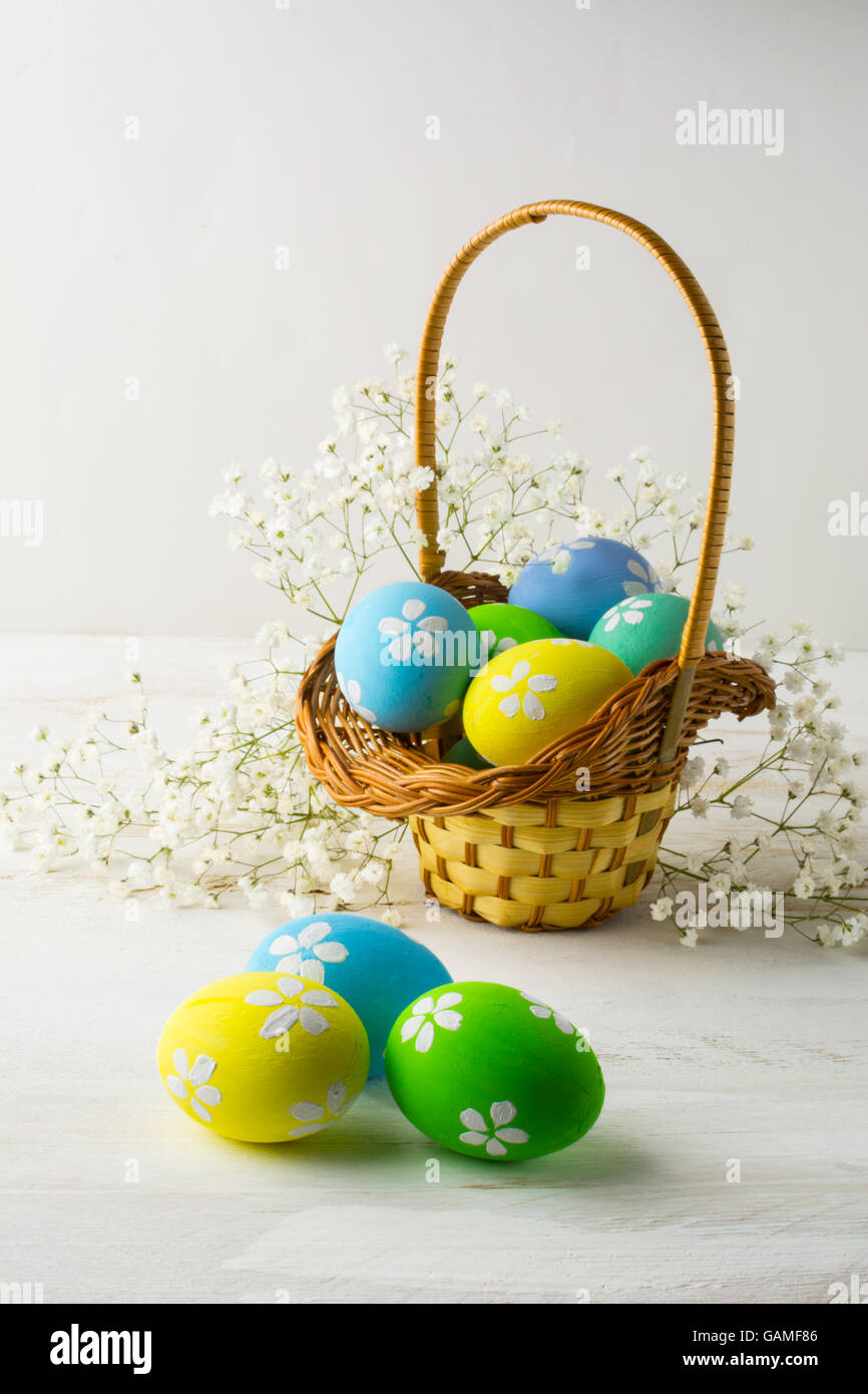 Decorated light blue, yellow, green Easter eggs in the basket with small white baby's breath flowers on a white wooden backgroun Stock Photo