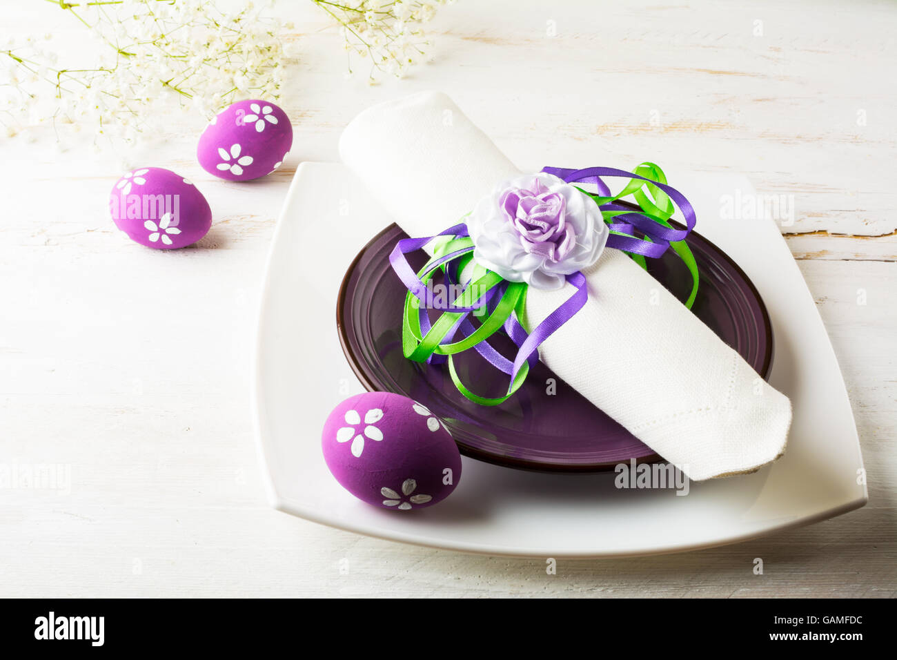 Purple mauve lilac Easter table place setting with plate, napkin and purple Decorated Easter eggs on white wooden background Stock Photo