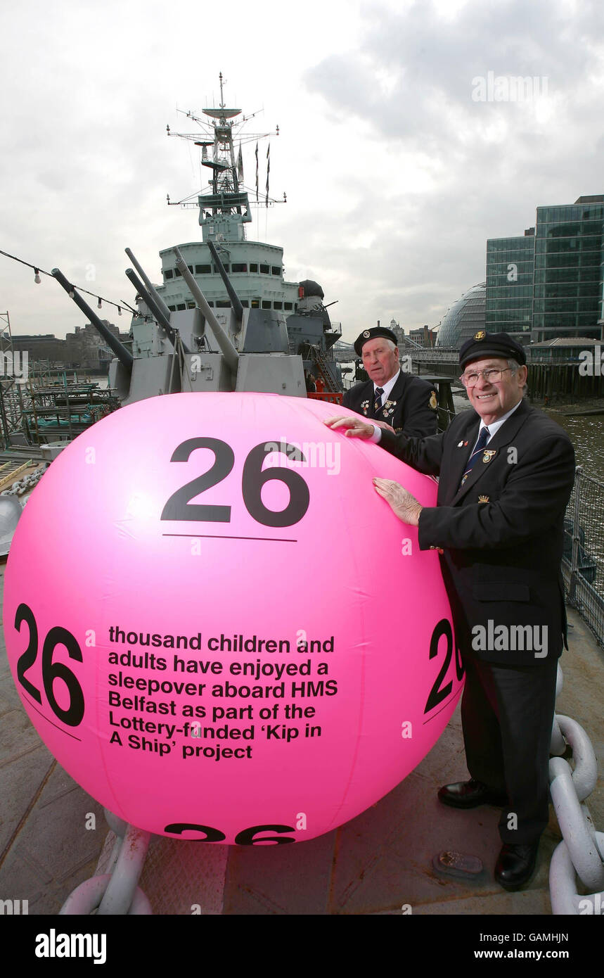Korean war veterans Bob Blackwell, 78, left and Ted Hill, also in his 70s, welcome a giant National Lottery ball aboard their former vessel, HMS Belfast, on the River Thames, London. Stock Photo
