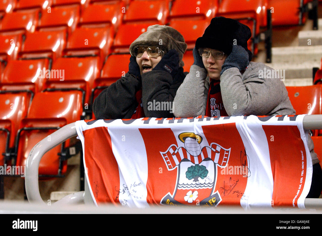 Two cold Southampton supporters cover their ears from the wind as they watch their team win 1-0 against Sunderland Stock Photo