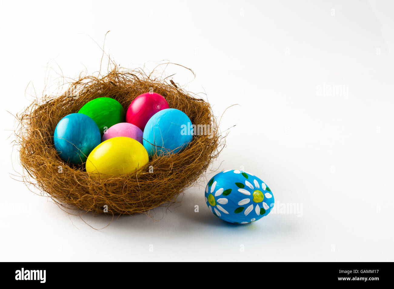 Multicolored Easter eggs in a nest and blue Easter egg with floral design on white background. Easter background. Easter symbol. Stock Photo
