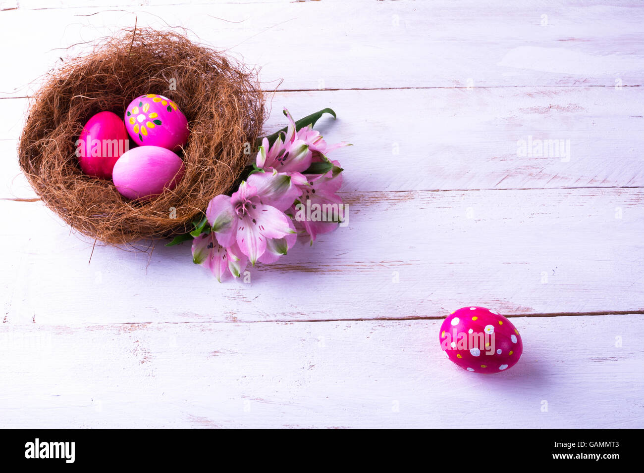 pink Easter eggs in a nest with soft pink flowers on the white wooden ...