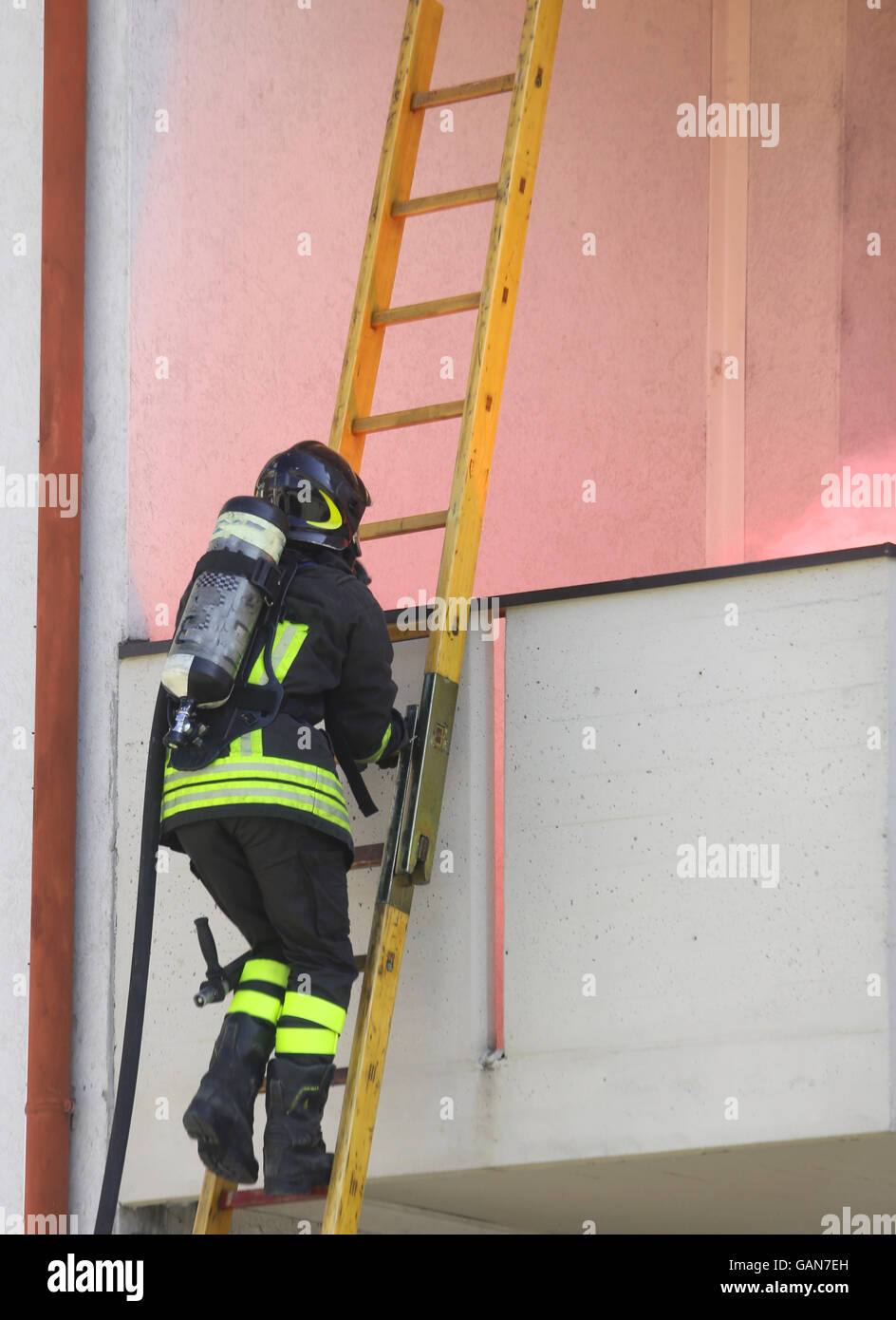 Firefighter with oxygen cylinder climbing a wooden ladder to put out the fire Stock Photo