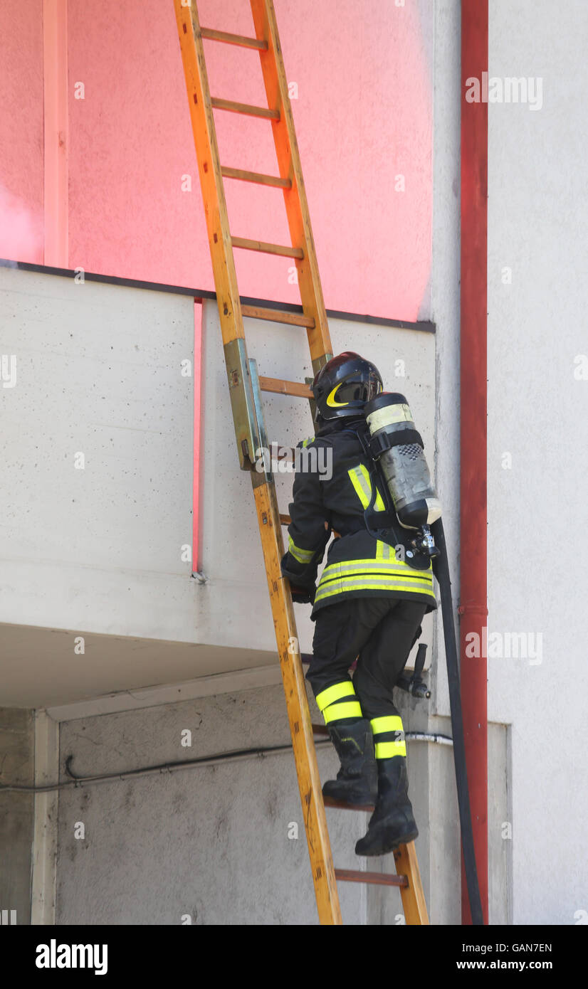 Firefighter with oxygen cylinder wood climbing a ladder to put out the fire Stock Photo