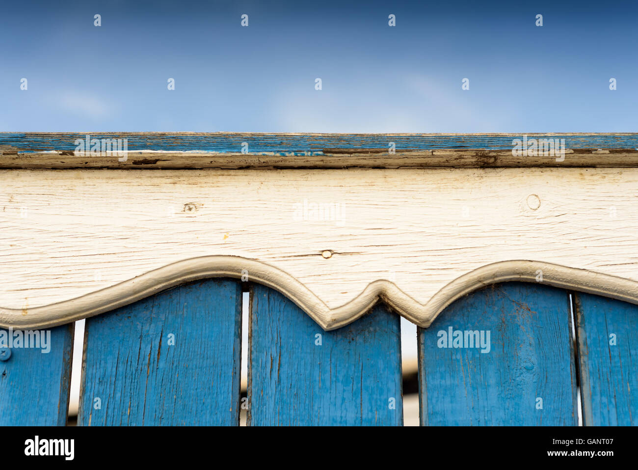 Intricate and ornate carved wooden detail rail on a blue painted fence with blue sky and copy space area. Stock Photo