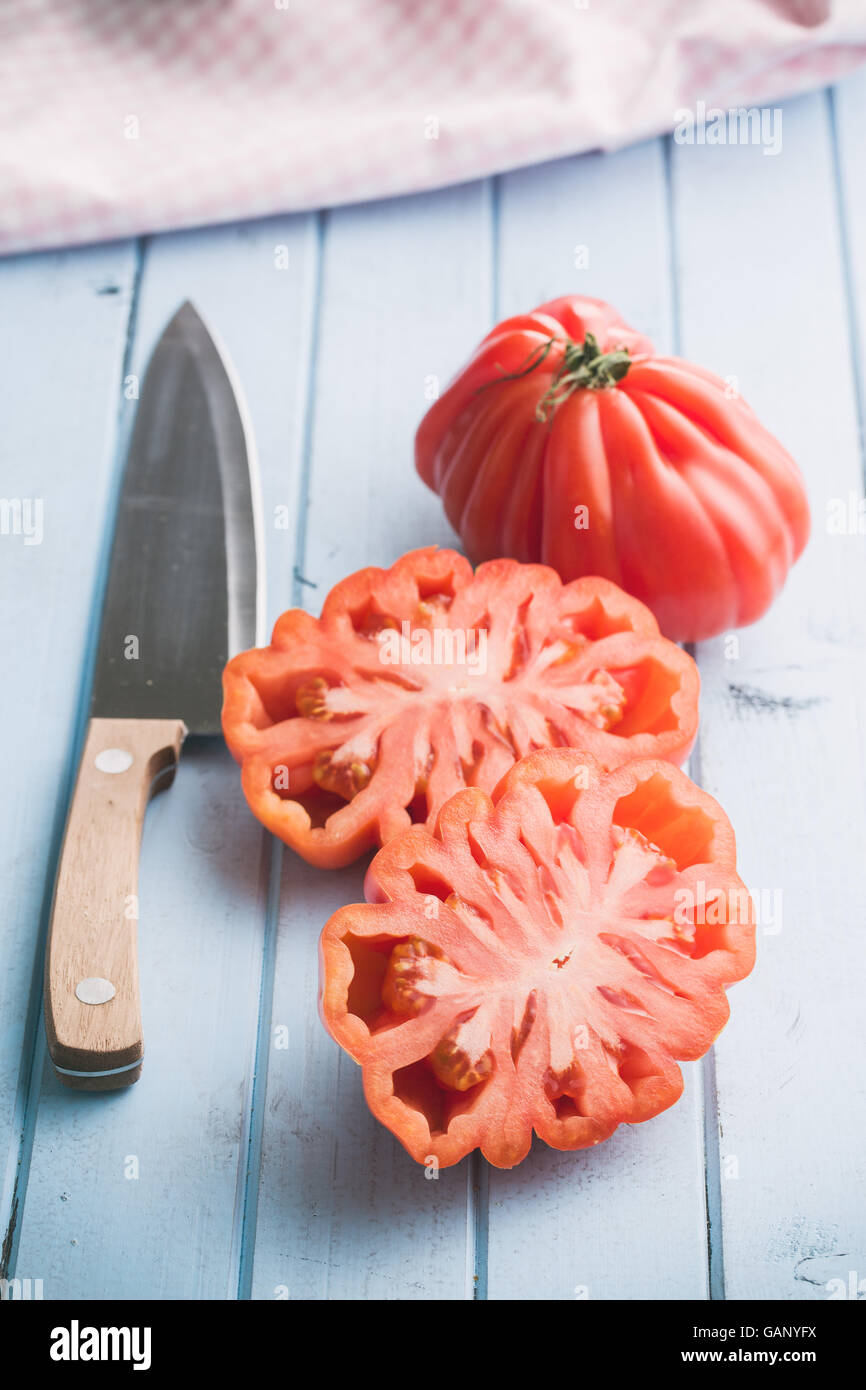 Coeur De Boeuf. Beefsteak tomatoes and knife on kitchen table. Stock Photo