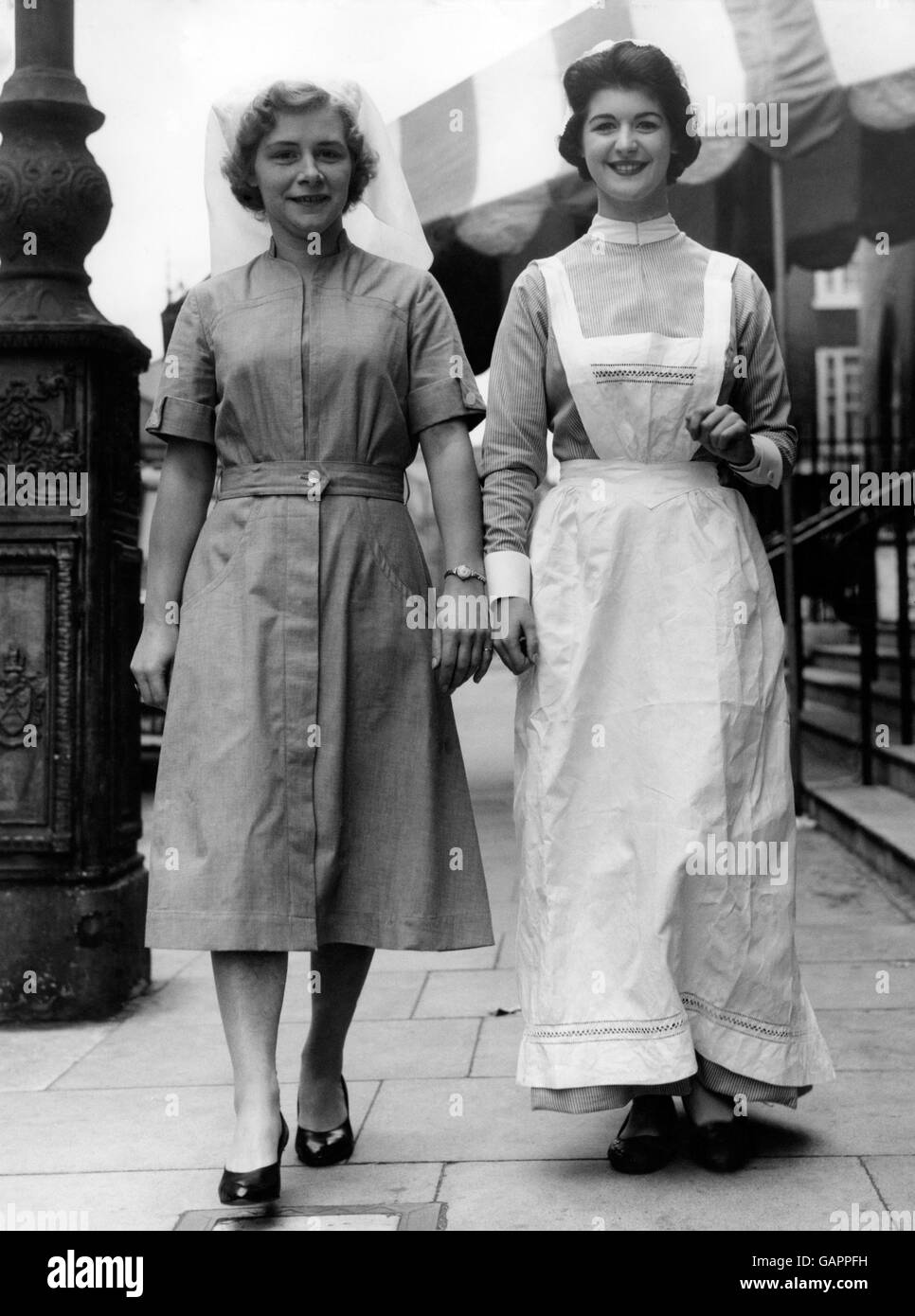 A striking contrast provided by two nurses' uniforms. At right is a uniform of the 1890s worn by model Pat Benton. On the left is a new 'easy-on, easy-off' uniform in blue viscose/cotton. Stock Photo