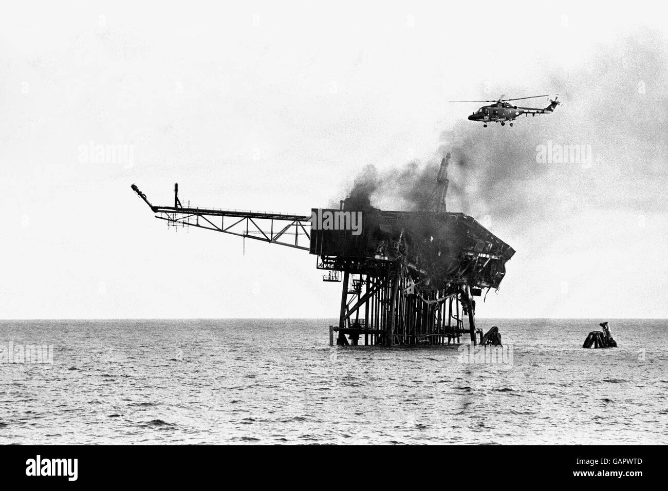 A rescue helicopter flies over the smouldering wreck of Piper Alpha, all that remains of the huge Occidental Oil rig which turned into a 'raging inferno' when an explosion ripped through the offshore platform yesterday. Stock Photo