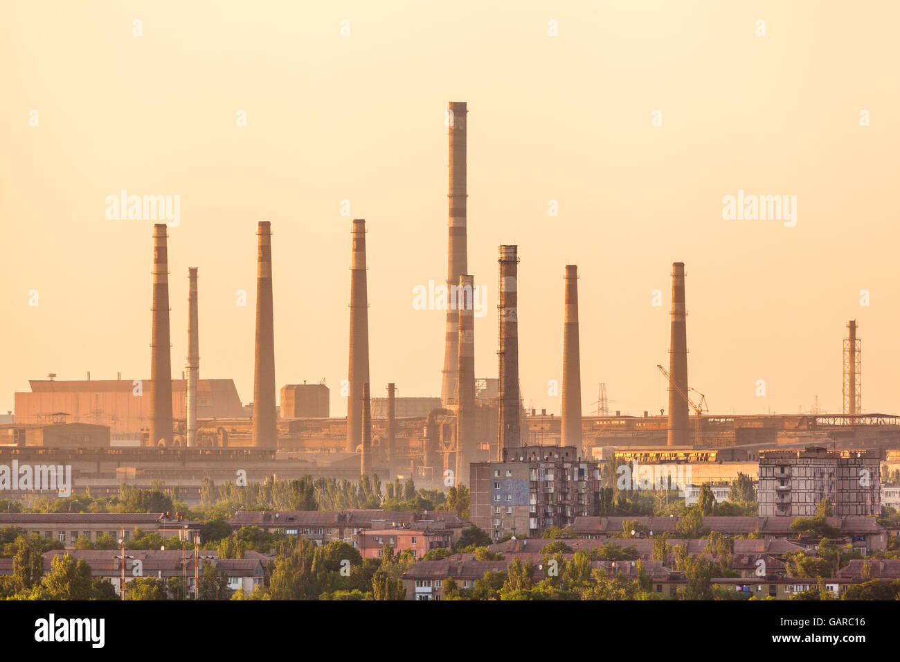 City buildings on the background of steel factory with smokestacks at colorful sunset. metallurgical plant. steelworks, iron wor Stock Photo