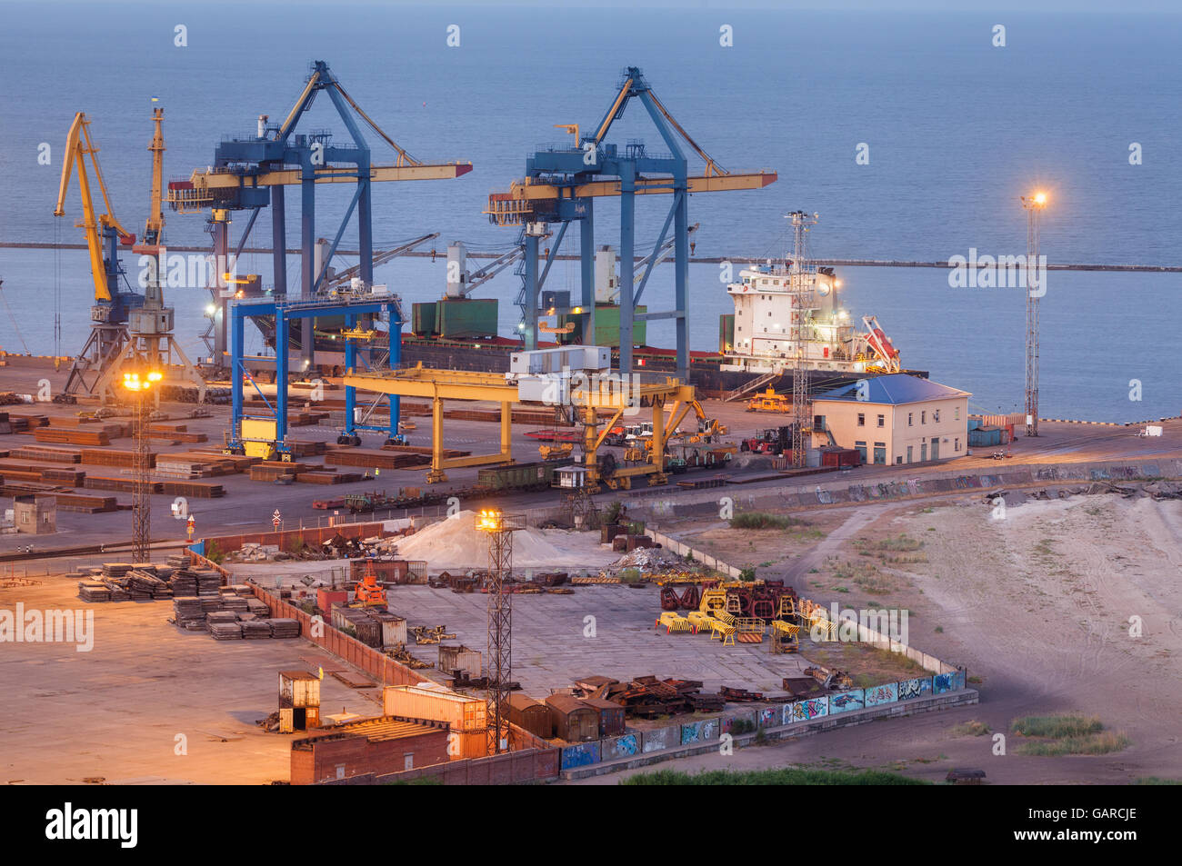 Sea commercial port at night in Mariupol, Ukraine. Industrial view. Cargo freight ship with working cranes bridge in sea port at Stock Photo