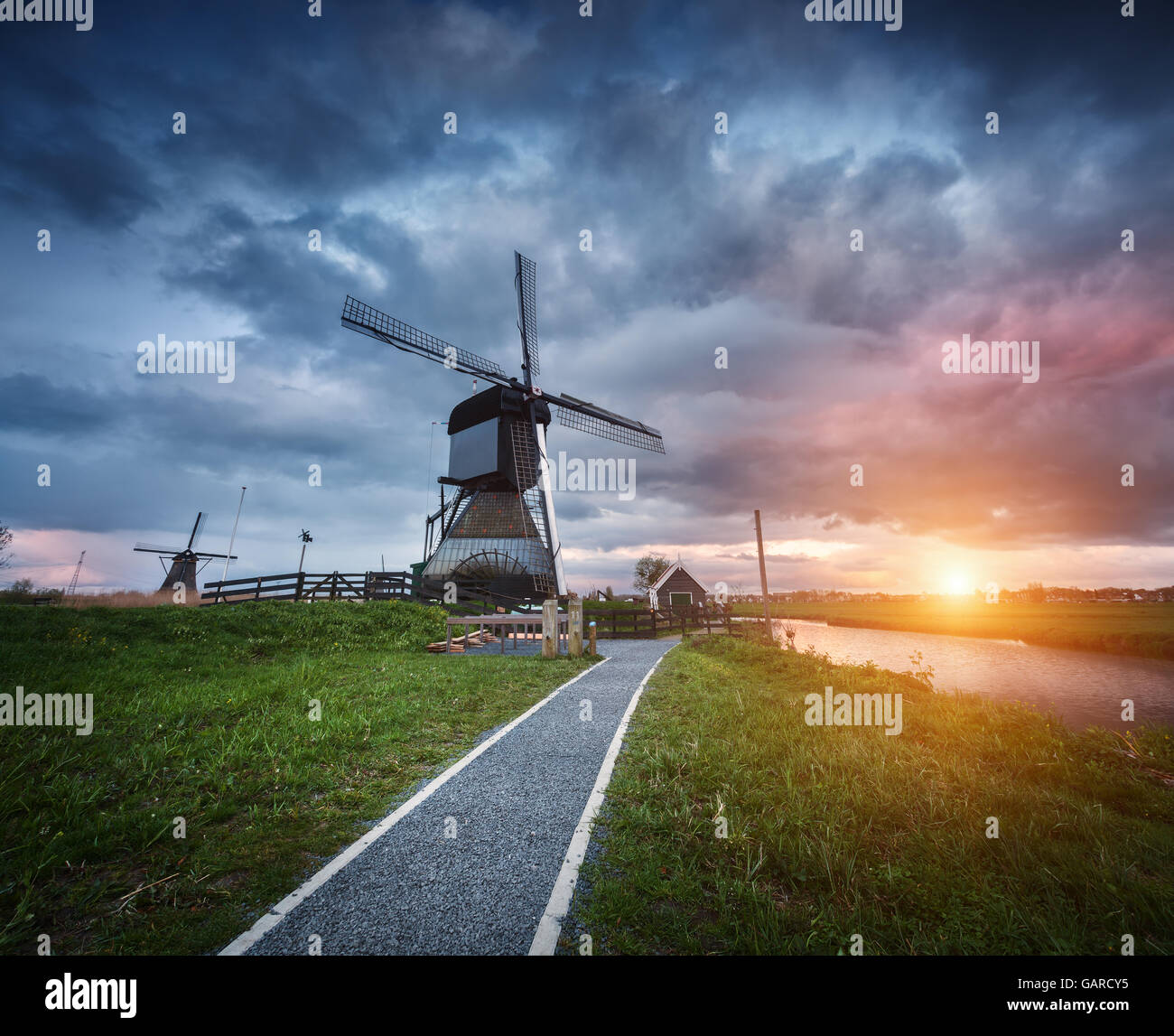 Landscape with traditional dutch windmills and path near the water canals. Clouds at colorful sunset in spring. Kinderdijk Stock Photo