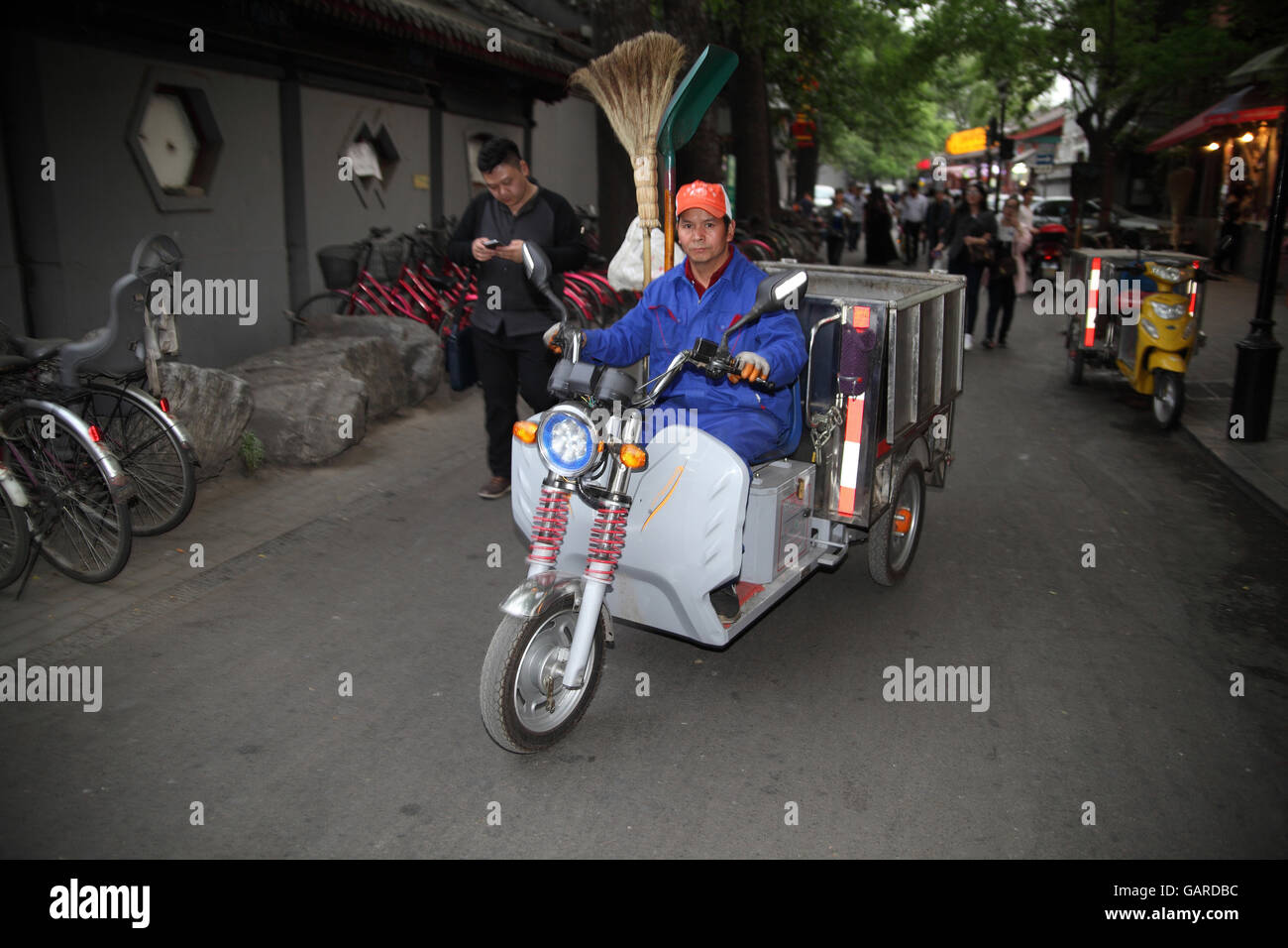 A Chinese cleaning worker riding a tricycle truck with cleaning stuff and a broom. By Houhai Lake, Beijing, China. Stock Photo