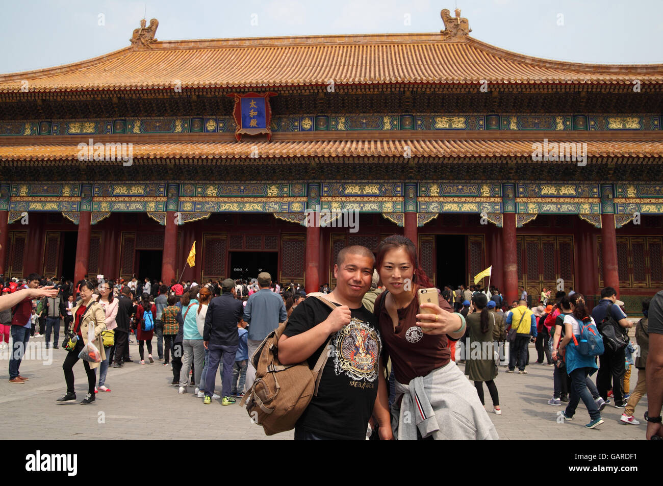 Woman uses a smartphone to take a selfie of her and her man in front of the Hall of Supreme Harmony, many tourists are around. Stock Photo
