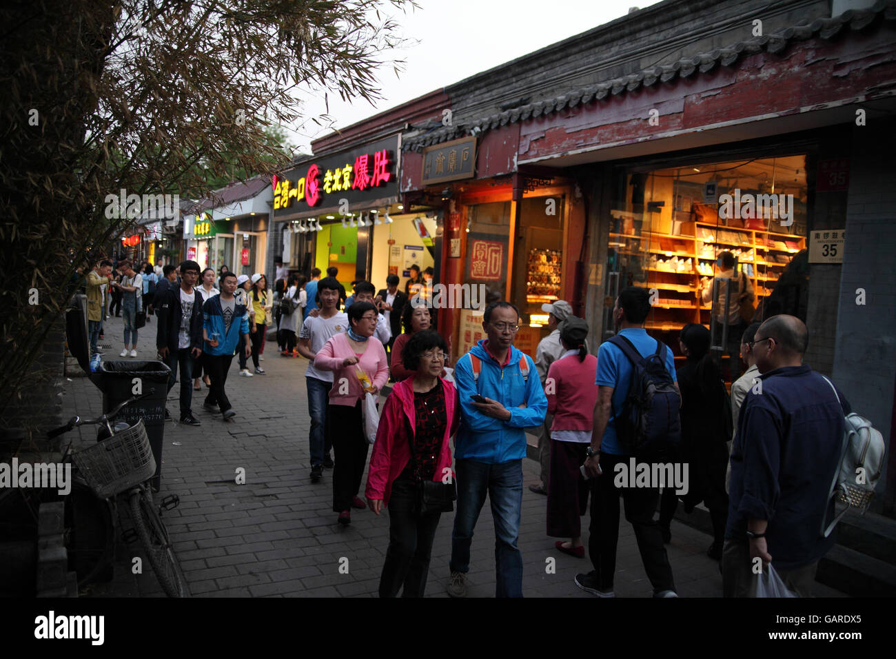 Chinese people and tourists walk in the evening in an alley of a historical hutong with lots of small shops. Nanluoguxiang Hutong, Beijing, China. Stock Photo