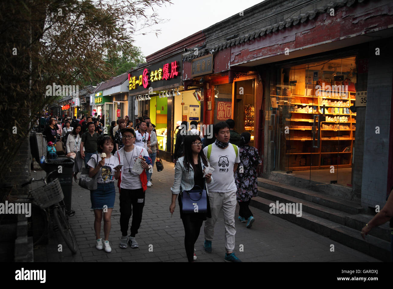 Chinese people and tourists walk in the evening in an alley of a historical hutong with lots of small shops. Nanluoguxiang Hutong, Beijing, China. Stock Photo