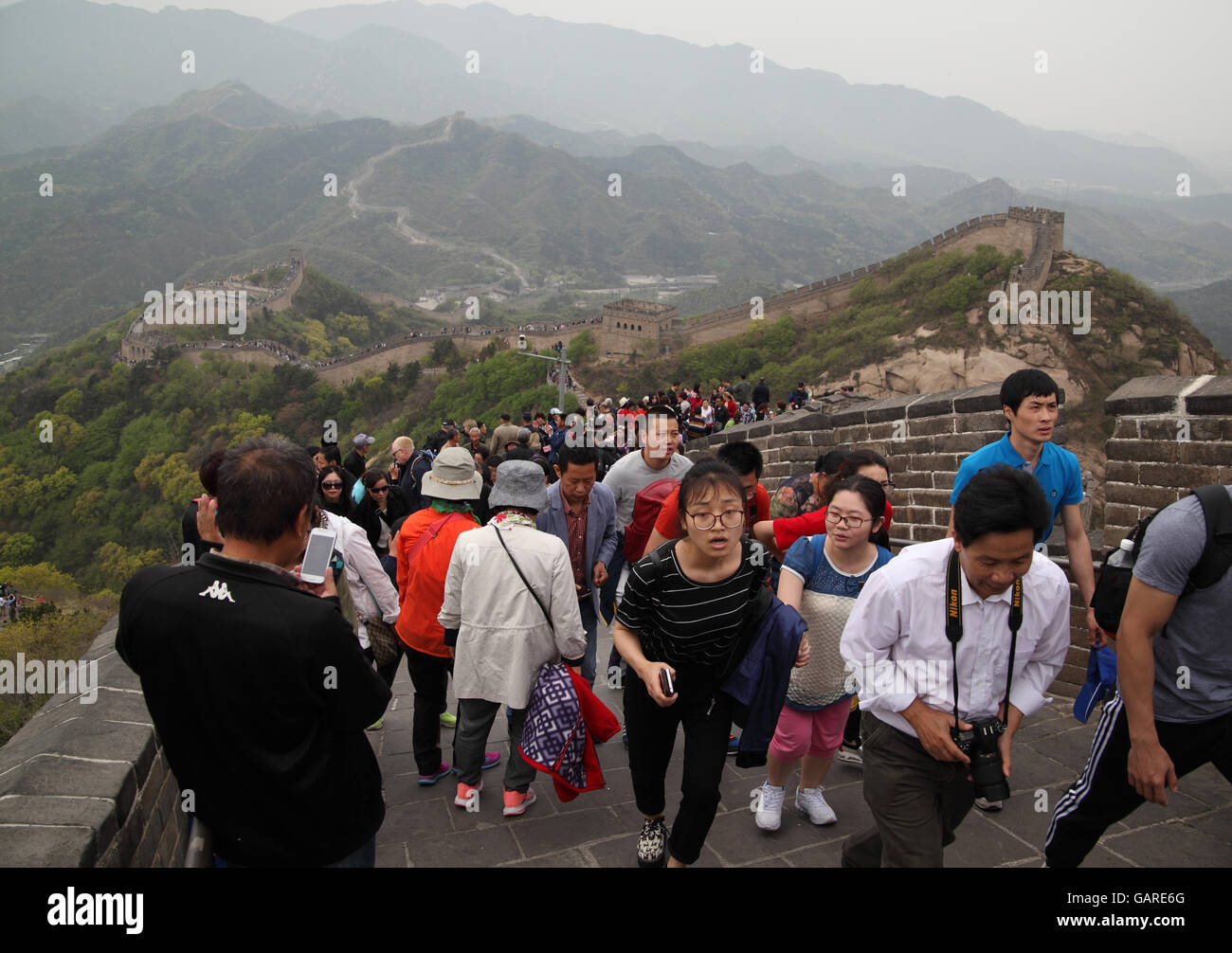 Lots of tourists, one takes photos with a smartphone, climb the Great Wall of China going along the rugged mountains. Badaling near Beijing, China. Stock Photo