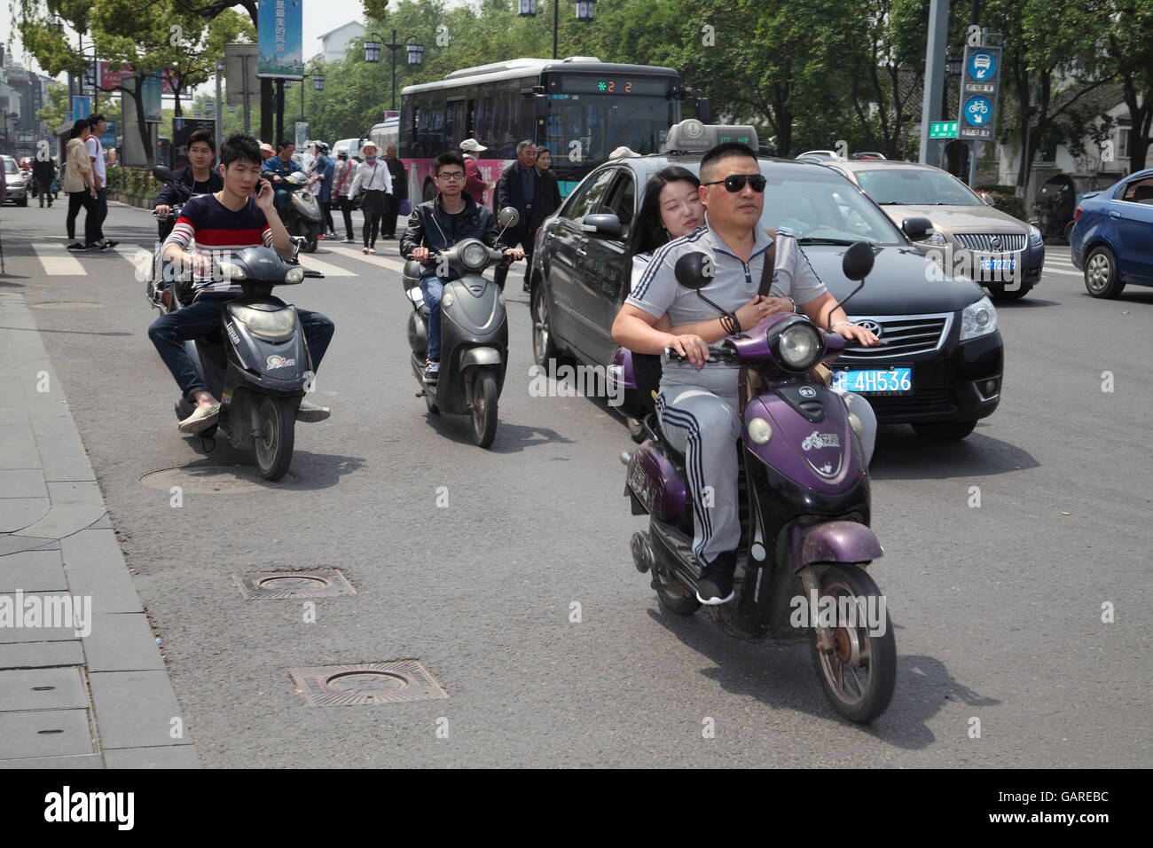 A Chinese traffic scene, motorbikes ride along cars, one rider uses his ...