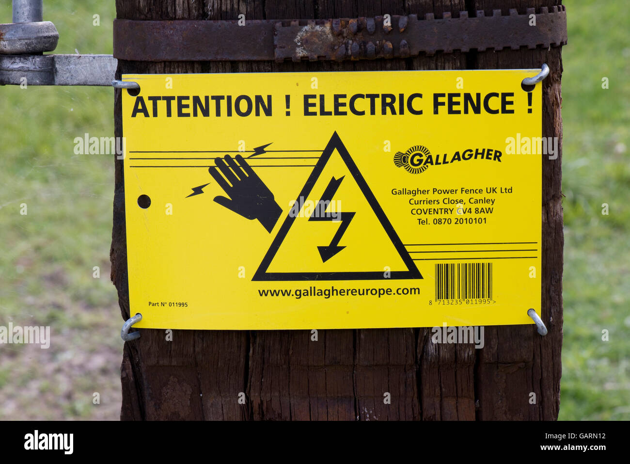 A sign warning of and electric fence surrounding a field of sheep "ATTENTION! ELECTRIC FENCE! Stock Photo