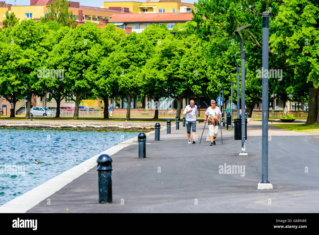 Motala, Sweden - June 21, 2016: Senior persons out for some exercise by the waterside promenade. Trees and the city behind them. Stock Photo