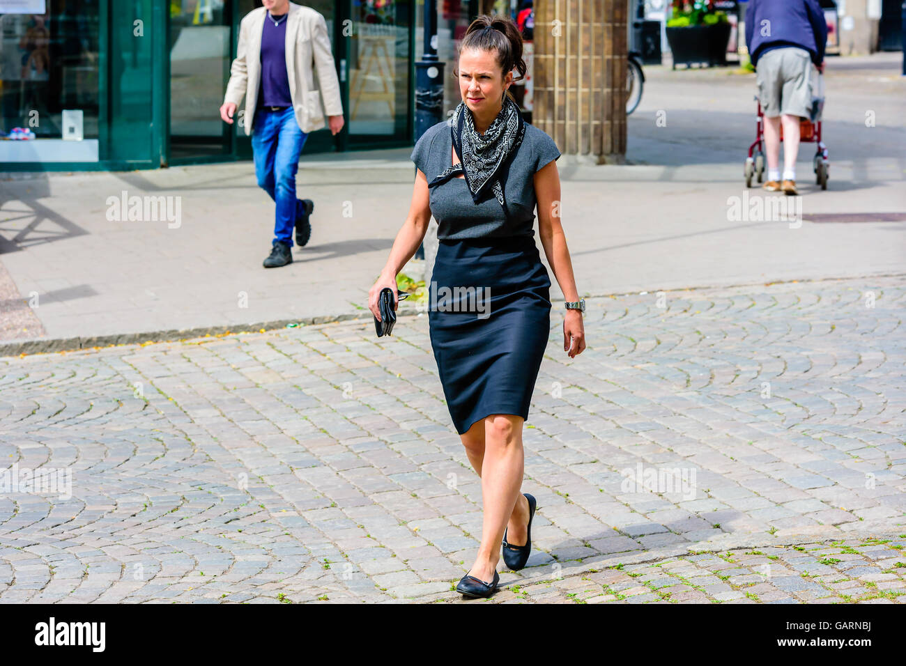 Motala, Sweden - June 21, 2016: Woman in skirt and blouse walking at a street in town. She also wears a scarf and ballerina shoe Stock Photo