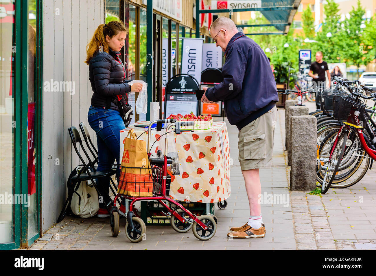 Motala, Sweden - June 21, 2016: Woman vending strawberries to a man outside a shop. Man has a walker standing beside him and he Stock Photo