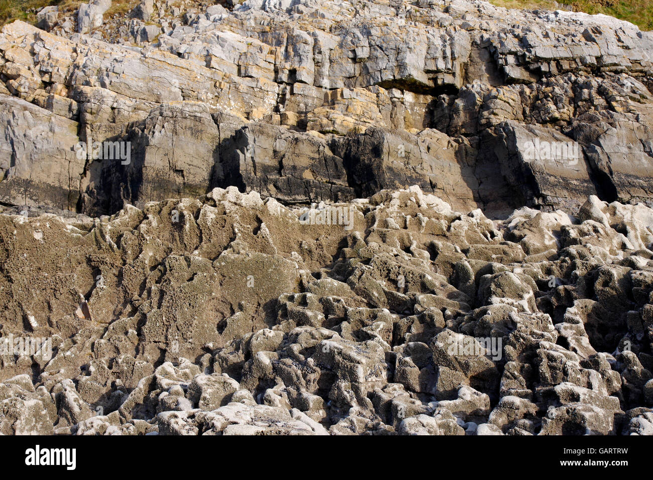 Coastal rocks eroded by the sea with a cliff in the background Stock Photo