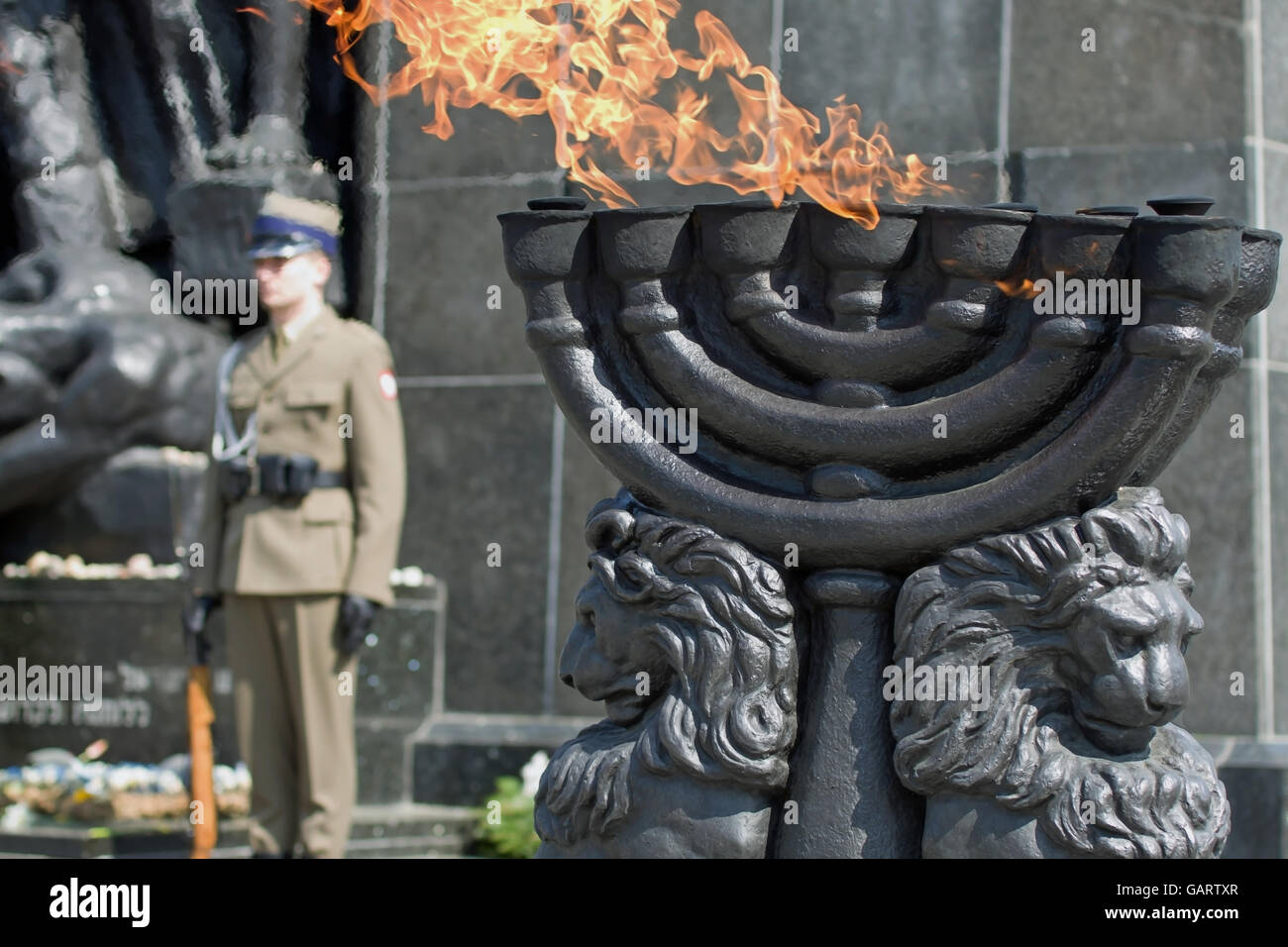 Menorah with burning flame in front of the Warsaw Ghetto Heroes Monument - Warsaw, Poland. Stock Photo