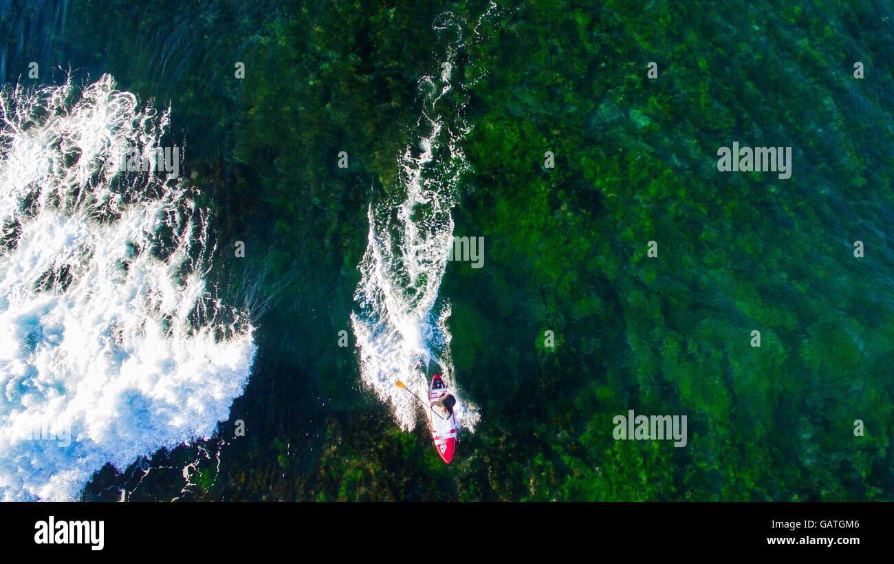 Aerial view of a man surfing on a stand up paddleboard SUP above algae covered rocks at Sandon Point, Bulli, NSW, Australia. Stock Photo