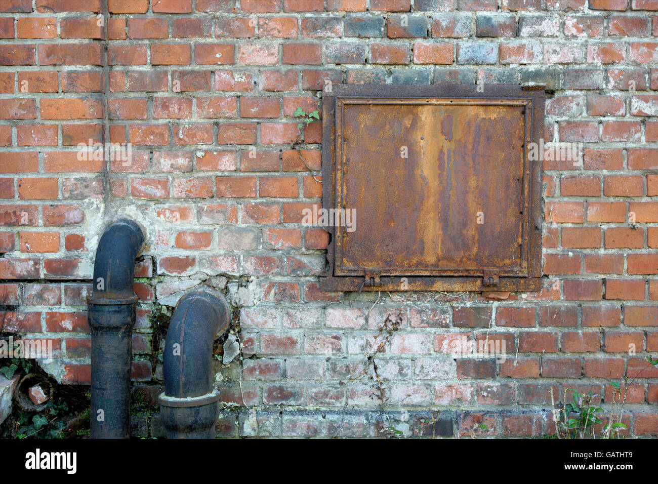 Brick wall of a old house with drainage pipes and one iron window Stock Photo