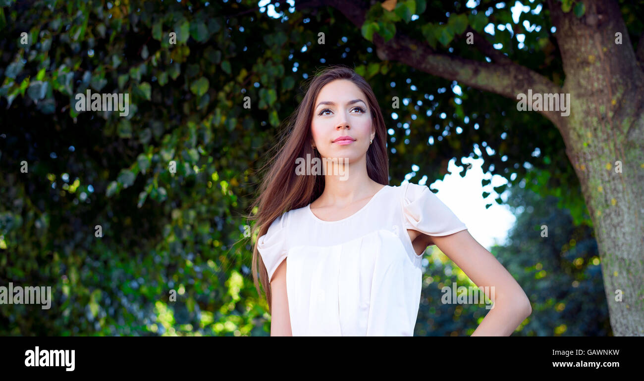 The girl in a pink dress, stands in the park and looks into the ...