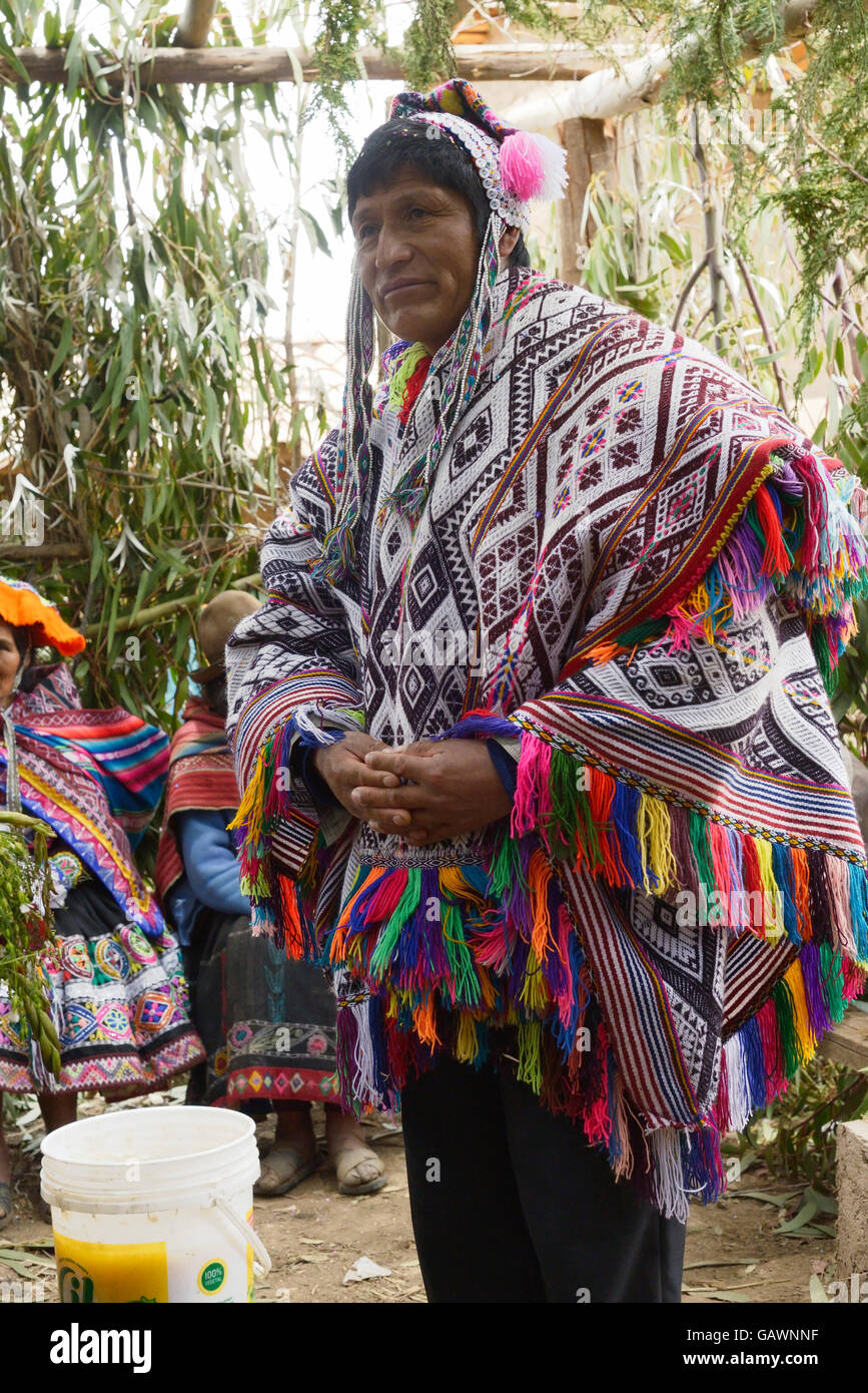 Native Peruvian man wearing a handwoven poncho and a chollo - knitted hat  with earflaps, attending his daughter wedding ceremony. Next to him is a  bucket with chicha - local beer derived