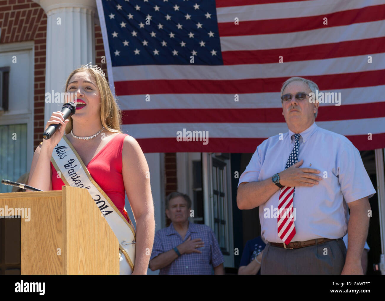 Wantagh, New York, USA. July 4, 2016.  KAYLA KNIGHT, Miss Wantagh 2014, sings God Bless America, with Hon. CHRISTOPHER QUINN standing to right of her and wearing red white and blue tie, at the start of the at the 60th Annual Miss Wantagh Pageant, an Independence Day tradition on Long Island. Judge Christopher Quinn is the Nassau County Supervising Judge of the County Court, and Acting Supreme Court Justice. Credit:  Ann E Parry/Alamy Live News Stock Photo