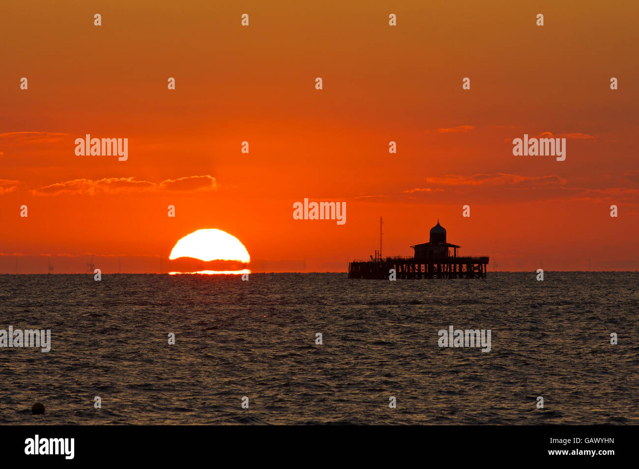 Herne Bay, Kent, UK. 6th July 2016: UK Weather. Sunrise gives the sky a red-orange glow over the remains of Herne Bay pier, which was so badly damaged by storms in 1978 that the central section was dismantled. The London array, the largest offshore windfarm in the world is seen through the heat haze. Temperatures could reach into the mid 20s at the weekend as hot air from the continent covers the south of the country Credit:  Alan Payton/Alamy Live News Stock Photo