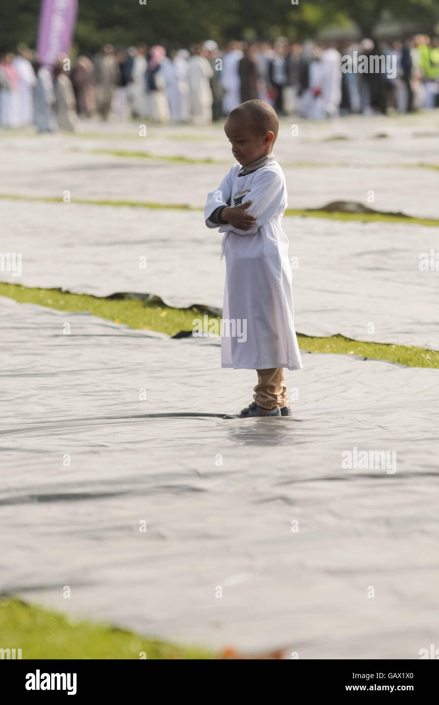 A little boy stands alone on the prayer mats during the Eid prayers in Small Heath park Birmingham 2016 Stock Photo