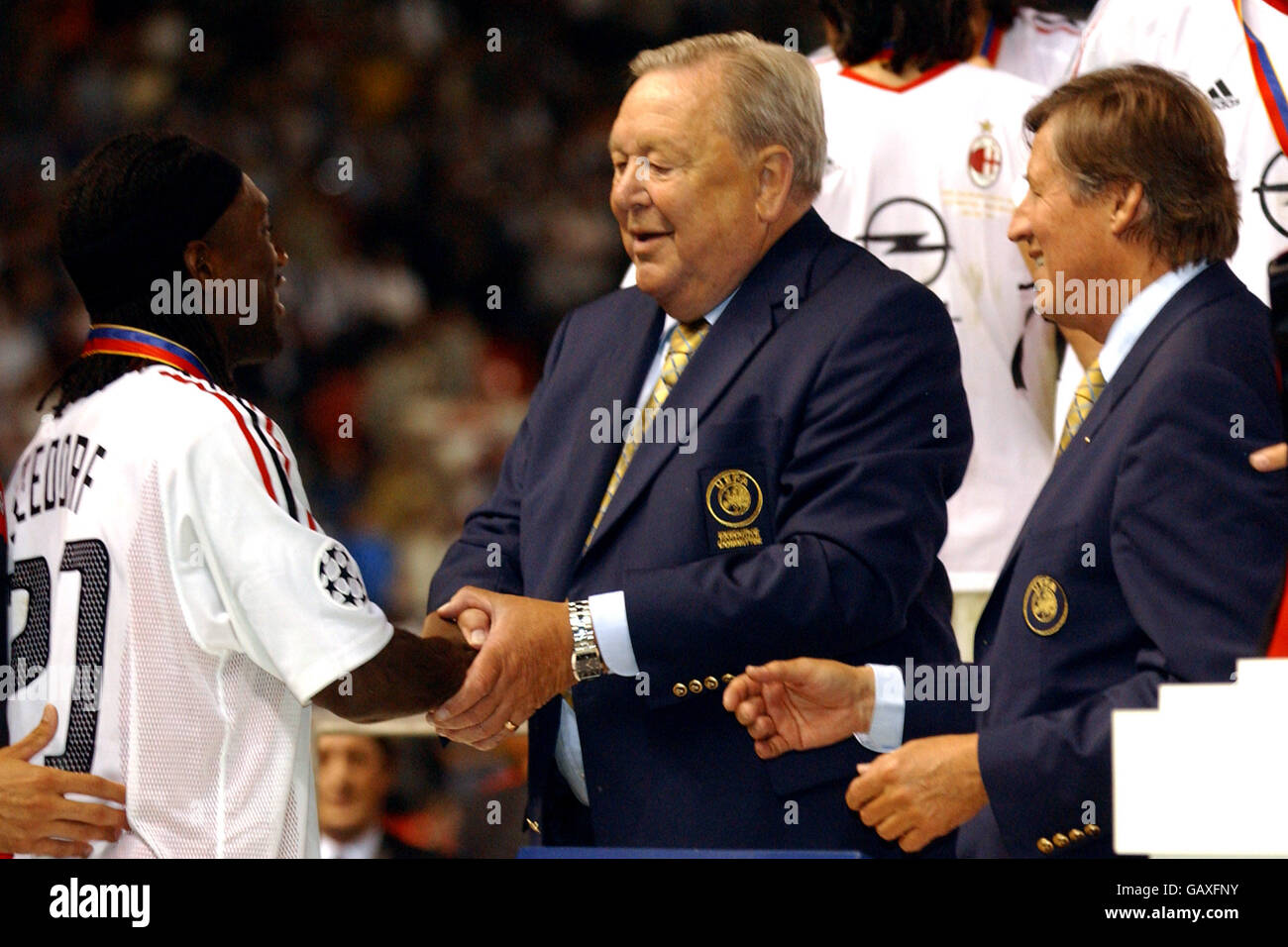 AC Milan's Clarence Seedorf (l) is presented with his winners medal by UEFA President Lennart Johansson and UEFA Chief Executive Gerhard Aigner (r) who congratulate him on becoming the first player to win the trophy for three different teams Stock Photo