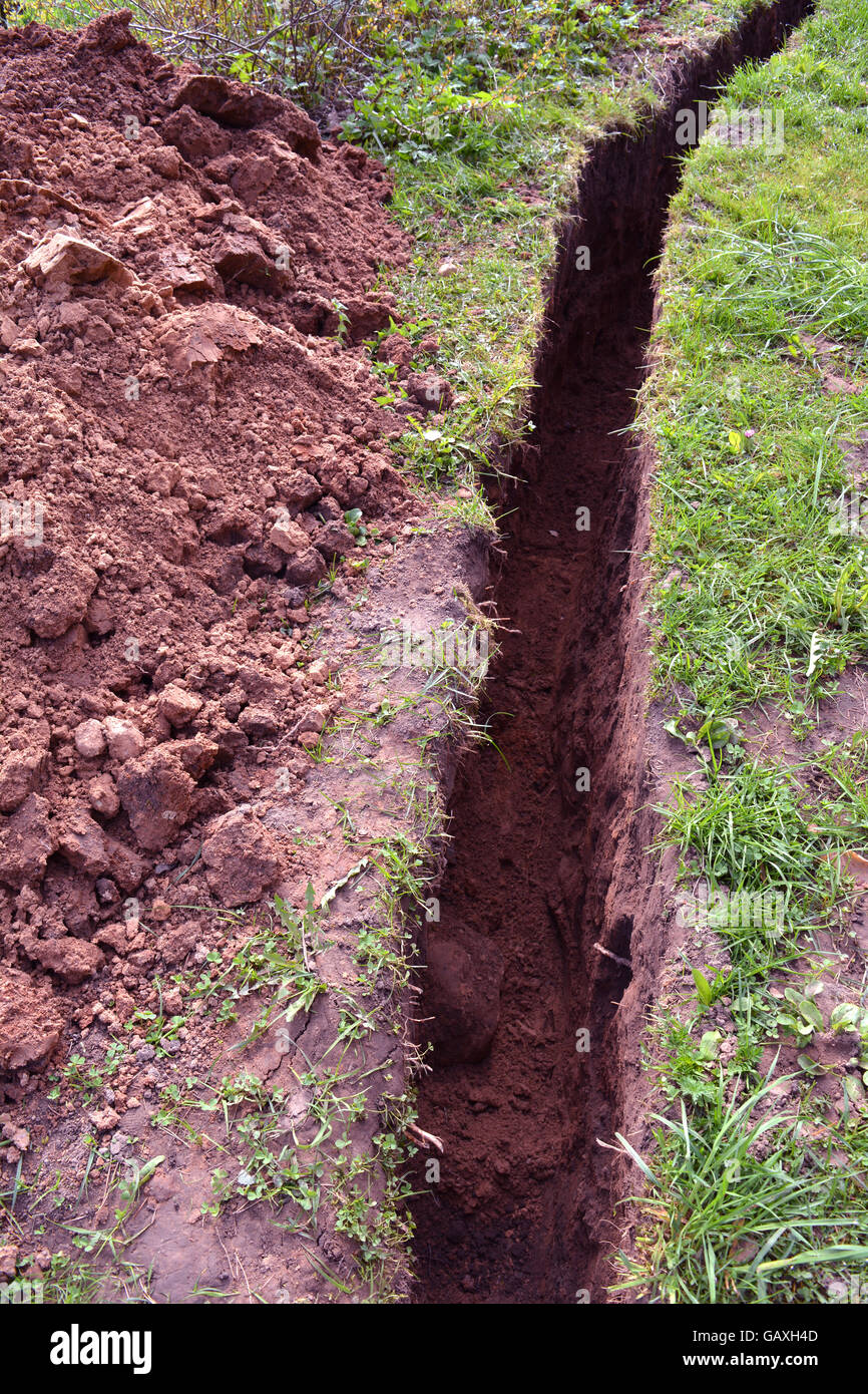 very narrow trench in summer farm yard through grass  for water pipe Stock Photo