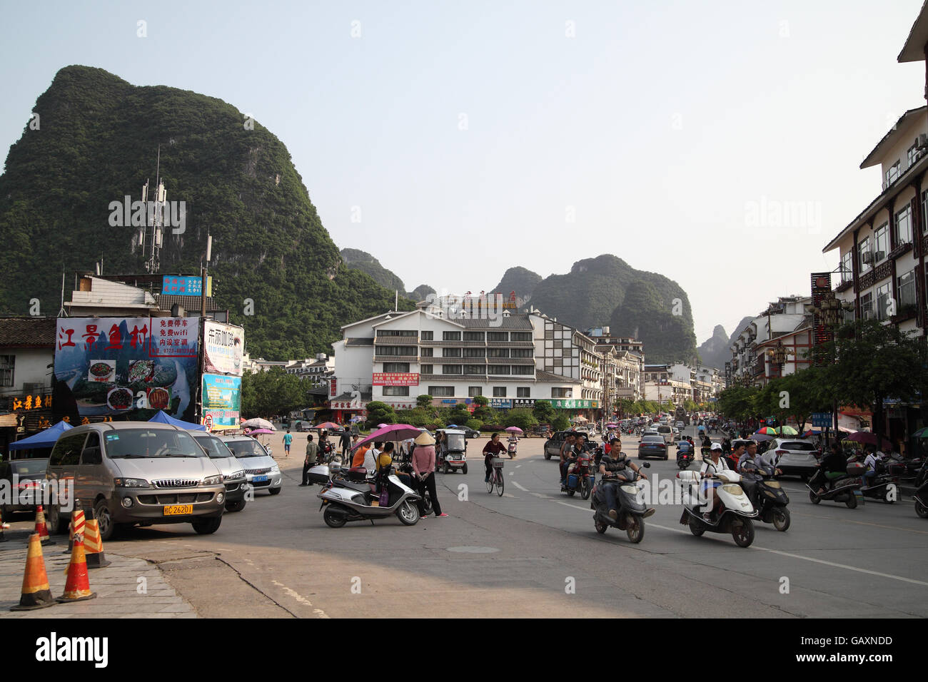 Cars, motorbikes and bicycles seen on a street, in the background are the Guilin area Karst hills and billboards in Chinese. Yangshuo, Guangxi, China. Stock Photo