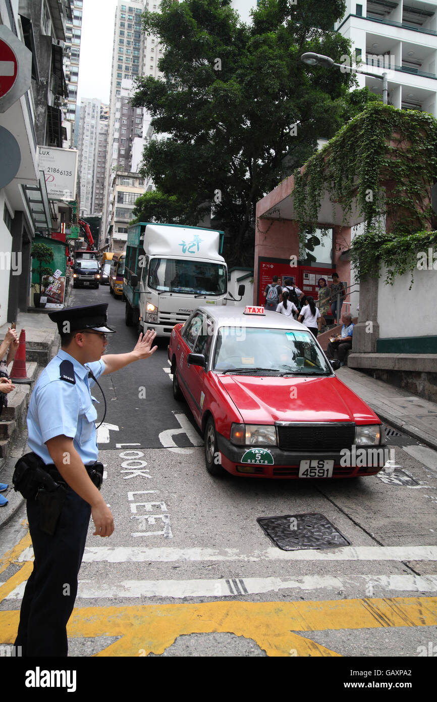 A Chinese policeman directing traffic gesturing cars to stop and wait at the cross road.. Hong Kong, Hong Kong. 06.05.2016. Stock Photo