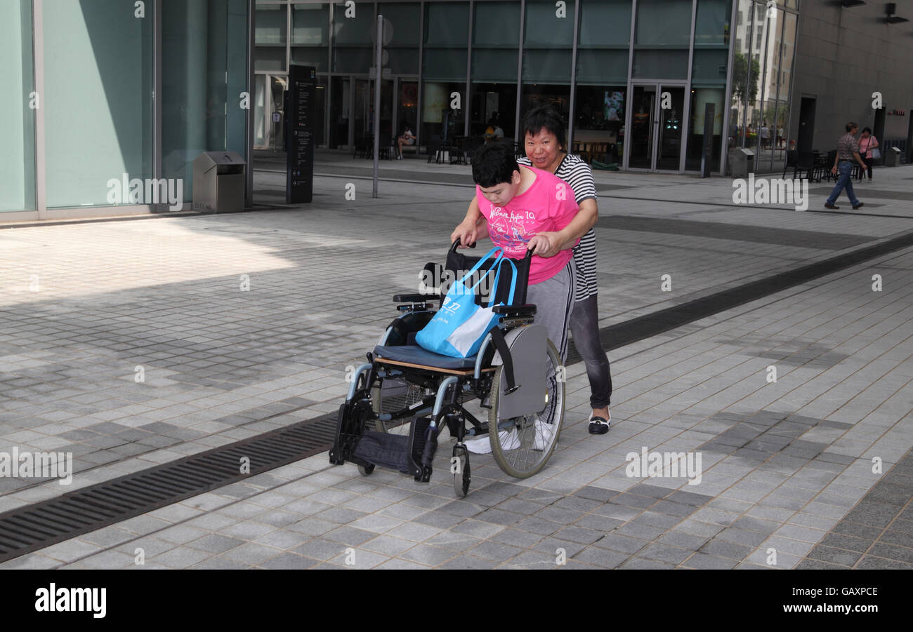 A 20 year old brain injured Chinese woman is helped by her mother to walk behind her wheelchair for exercise, they do it daily Stock Photo