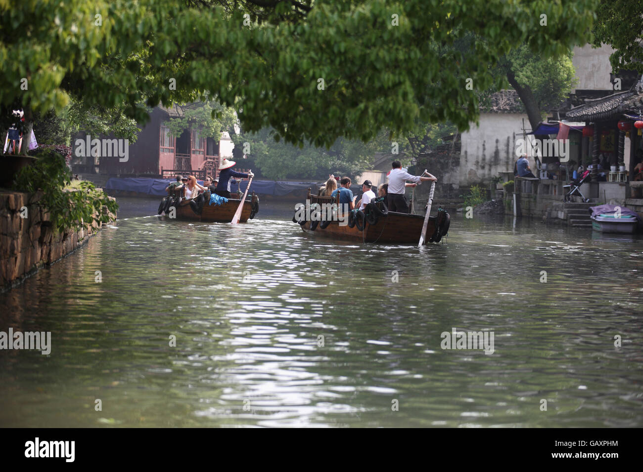 Tourists ride in row boats in a canal in an ancient town in China, a woman is rowing one of  the boat a man is rowing the other Stock Photo